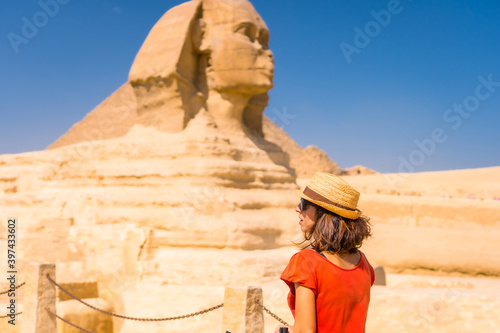A young tourist at the Great Sphinx of Giza dressed in red and with a hat, from where the miramides of Giza. Cairo, Egypt