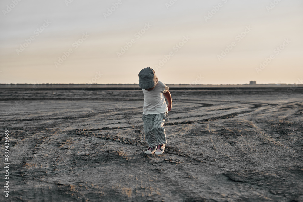 Two-year-old child in a hat walks along a country road, summer. Knowledge of the world. Two-year-old child in a hat walks along a country road, summer. Knowledge of the world.
