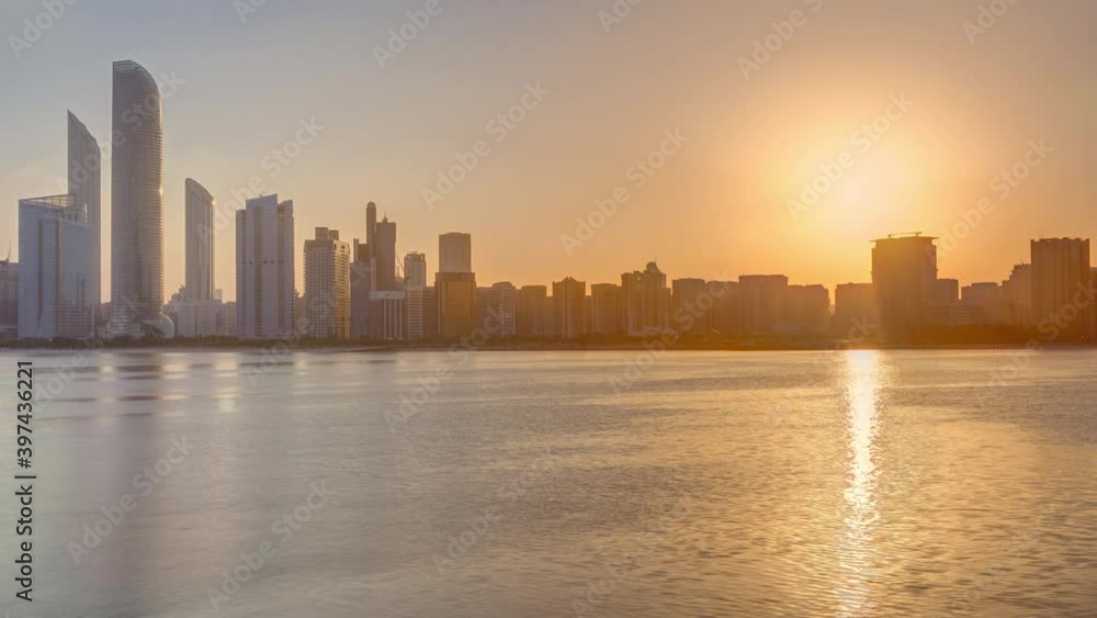 Abu Dhabi city skyline on sunrise time with water reflection timelapse from the breakwater near cultural village. Few clouds on morning sky Abu Dhabi city skyline on sunrise time with water reflection timelapse from the breakwater near cultural village. Few clouds on morning sky