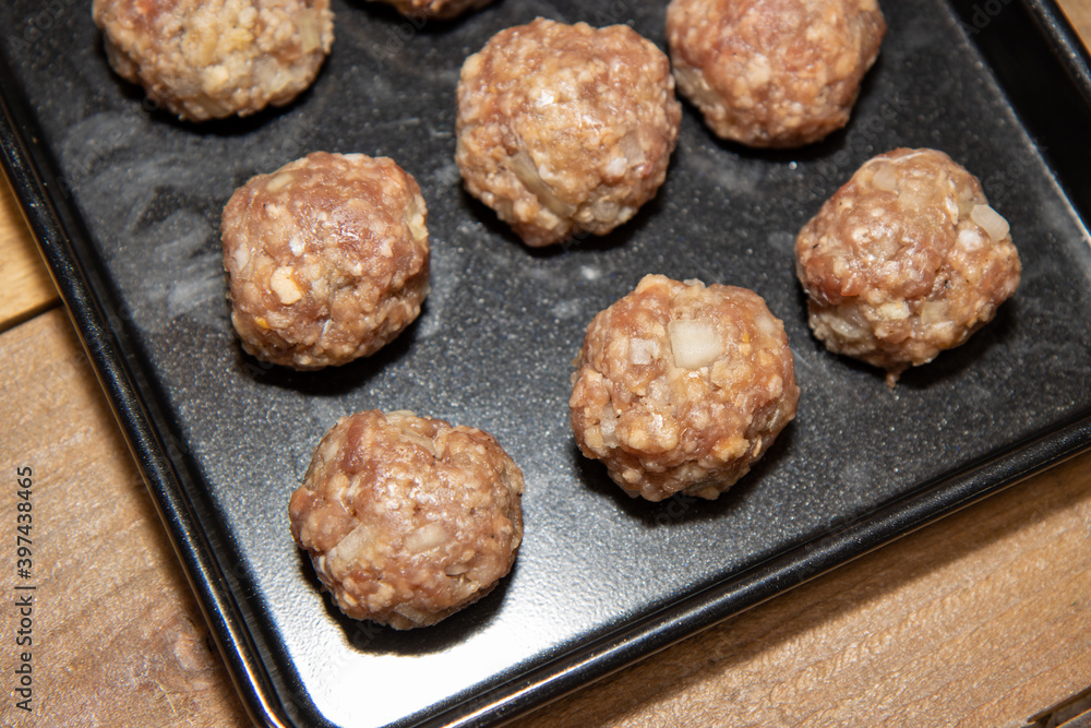 Raw uncoooked beef meat balls on a baking trey ready to be put in the oven