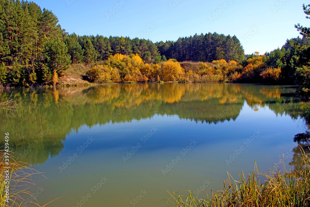 In the still surface of the water of the amazing lake, trees and the sky are reflected as in a mirror.