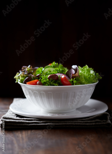 Salad with cherry Tomatoes, Cucumber, Lettuce and Kalamata Olives on dark wooden Background. 