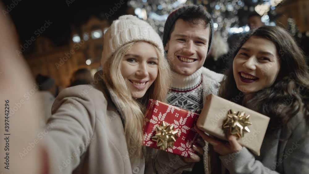 Selfie portrait of group of teenagers smiling and having great time on christmas eve outside. Girls kissing guy friend, exchanging presents on street of european town. Selfie portrait of group of teenagers smiling and having great time on christmas eve outside. Girls kissing guy friend, exchanging presents on street of european town.