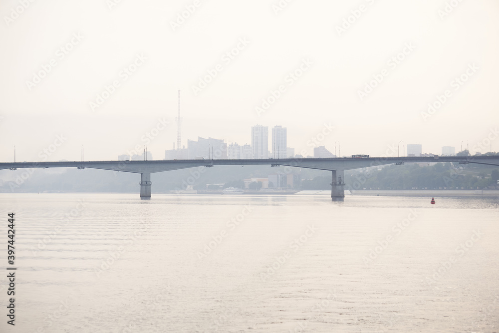 road bridge over a wide river and the silhouette of a distant city behind it in the morning fog