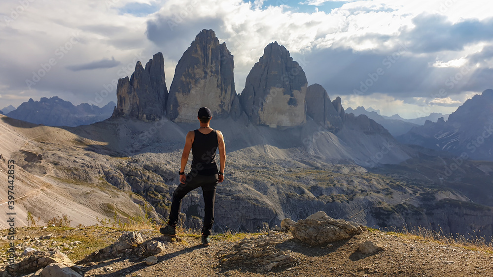 Fototapeta premium A man in hiking outfit standing on top of Sextner Stein and enjoying the view on the famous Tre Cime di Lavaredo (Drei Zinnen), mountains in Italian Dolomites. Desolated and raw landscape. Freedom