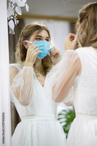 The bride in the medical mask looks in the mirror.