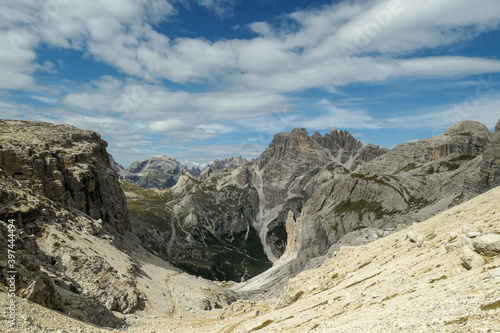 A panoramic view on Dolomites in Italy. There are sharp and steep mountain slopes around. Lots of lose stones and pebbles. The sky is full of soft clouds. Raw landscape. Serenity and calmness