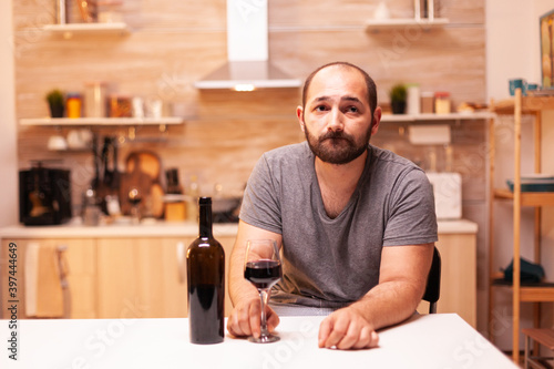 Thoughtfull young man holding a glass of red wine thinking about life problems. Unhappy person disease and anxiety feeling exhausted with having alcoholism problems.