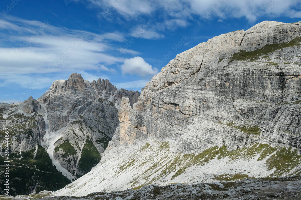 Fototapeta premium A panoramic view on Dolomites in Italy. There are sharp and steep mountain slopes around. Lots of lose stones and pebbles. The sky is full of soft clouds. Raw landscape. Serenity and calmness