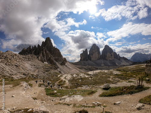 Panoramic view on a valley in Dolomites, Italy. There are sharp and steep mountain slopes around. Lots of lose stones and pebbles. The sky is full of soft clouds. Raw landscape. Serenity and calmness