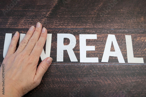 Фототапет hand changes the word unreal to real on wooden background, closeup