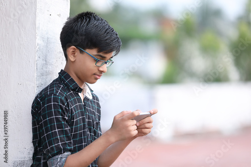 Portrait of Indian young boy playing game using mobile phone at home terrace