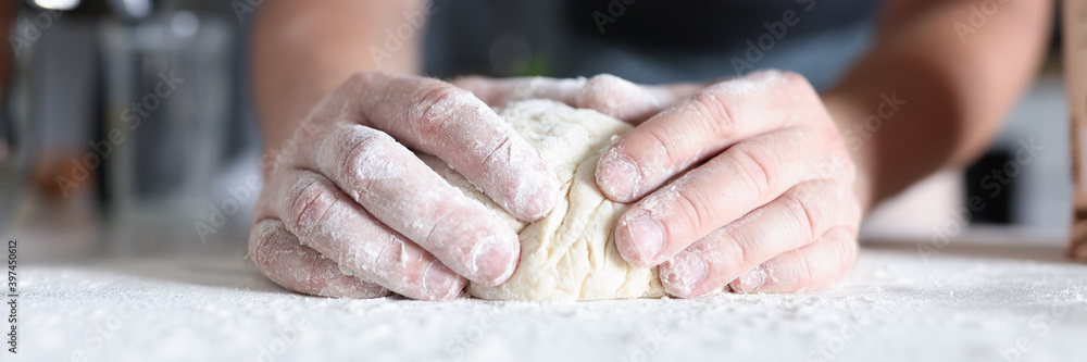 Male hands prepare dough in kitchen. Dough in flour on table close-up. Male hands prepare dough in kitchen. Dough in flour on table close-up.
