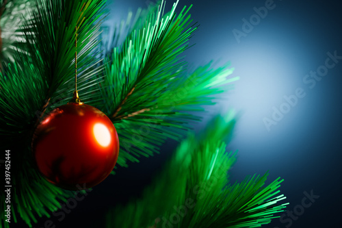 Close-up of a red shiny Christmas ball hanging on a Christmas tree in the background a lot of garlands glowing in different colors. New Year and Christmas concept. Beautifully decorated Christmas tree