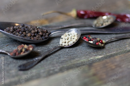 Different types of pepper in vintage metal spoons on old wooden background