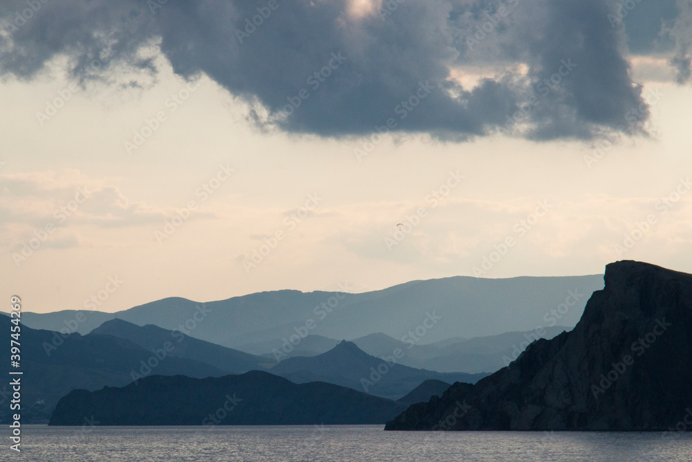 Scenery. Sunset. In the foreground is the sea. Further mountains, gray clouds in the light sky. Dark. Scenery. Sunset. In the foreground is the sea. Further mountains, gray clouds in the light sky. Dark.
