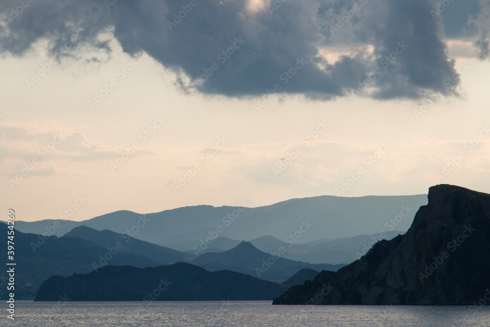 Scenery. Sunset. In the foreground is the sea. Further mountains, gray clouds in the light sky. Dark.