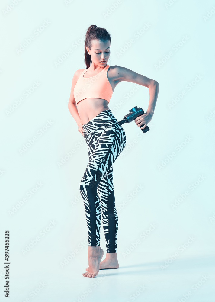 Percussion massager, young athletic female massaging buttock, hip, post-workout recovery routines, photo with copy space Percussion massager, young athletic female massaging buttock, hip, post-workout recovery routines, photo with copy space