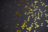 Golden star shape confetti pattern on black background. Christmas, New Year, magic concept. Close-up, copy space.