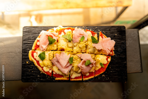 italian bruschetta close up during aperitivo. italian bread with tomato sauce and mozzarella with ham with natural light indoor in a bar, with hands serving it on table photo