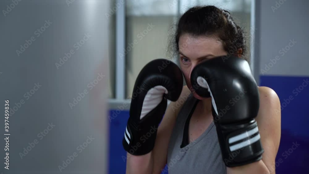Woman in boxing gloves training with punching bag in gym. Female boxer working out and breathing hard. Concept of sport Woman in boxing gloves training with punching bag in gym. Female boxer working out and breathing hard. Concept of sport