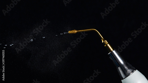 dental gilded nozzle with jet of water, shot against a black background