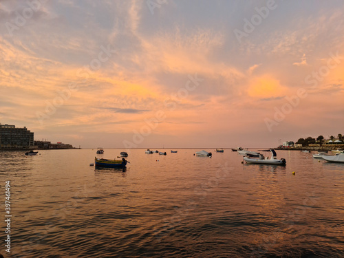 The setting sun over Saint Julians Bay turns the clouds and sea a golden colour, there are boats moored in the bay in between Saint Julian's and Sliema, Malta.