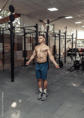 Muscular sport man with a naked torso jumps on a skipping rope in a modern cross gym. Cartio workout, healthy lifestyle