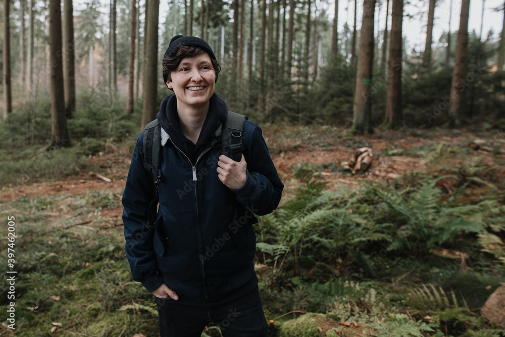 personable person in an impressive, beautiful forest laughs naturally. Young modern hipster tourist in nature while hiking.