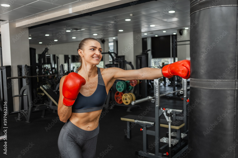 Fit woman boxer trains hand punch with punching bag in the gym