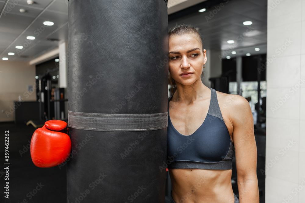 Woman boxer, tired after intense workout, hugs punching bag