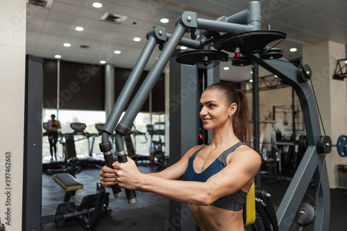 Young fitness woman working out in fly exercise machine in the gym