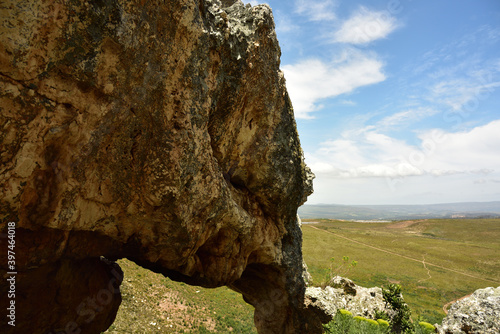 A huge rock shaped like an elephant against a green flied, blue sky and clouds