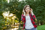Young cheerful funny woman listens to music with headphones in the park at sunrise.