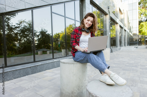 Young cheerful woman student using laptop outdoors. Distance work or education concept