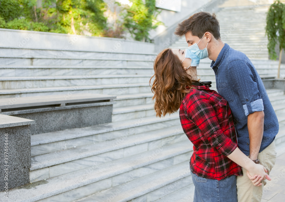 Fototapeta premium Young Couple in love, man and woman kissing each other in protective medical mask on face outdiir. Environmental pollution concept. Pandemic coronavirus( covid-19), virus protection