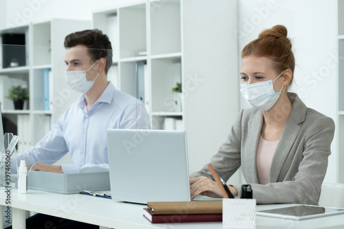 Young pretty businesswoman in protective mask and grey suit analyzing data