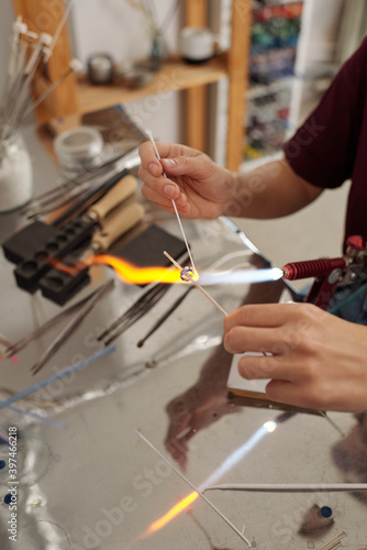 Hands of young female professional lampworker burning glass workpiece with fire