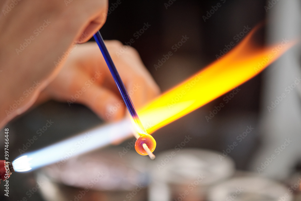 Creative female artisan burning glass workpiece while holding it close to fire Creative female artisan burning glass workpiece while holding it close to fire