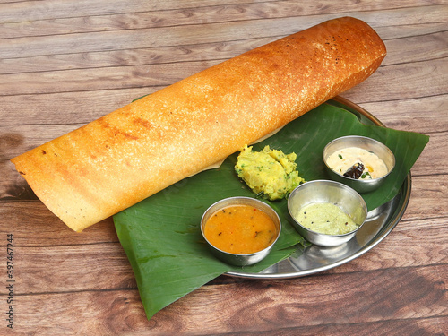 Masala dosa, a south Indian traditional and popular crepe with filling of a mixture of mashed potatoes and fried onions served with chutney and sambar over a rustic wooden background, selective focus