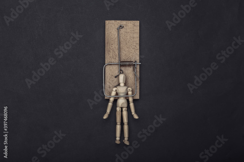 Wooden puppet caught by a mousetrap on a black background