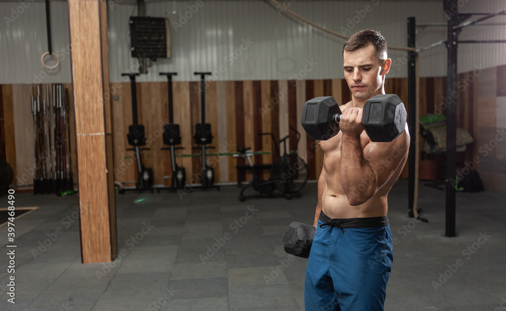 Muscular man is exercising with heavy dumbbells, training biceps in the gym. Healthy lifestyle Muscular man is exercising with heavy dumbbells, training biceps in the gym. Healthy lifestyle