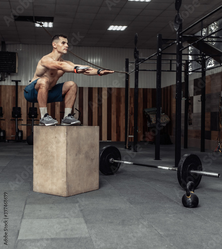 Muscular male athlete is practicing jumping on a wooden box in modern health club. Cross, functional training © splitov27