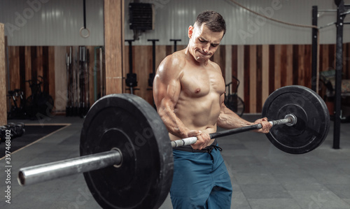 Muscular man with a naked torso training biceps with a heavy barbell in a modern health club. Bodybuilding and Fitness