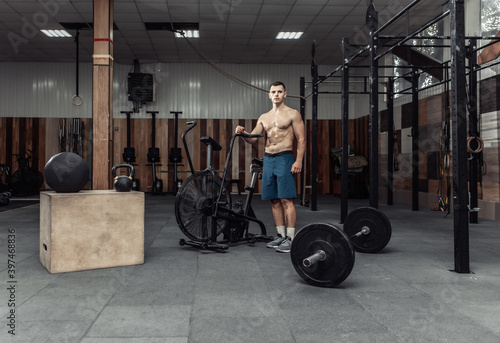 Muscular male bodybuilder posing in modern cross fit club with equipment for functional training