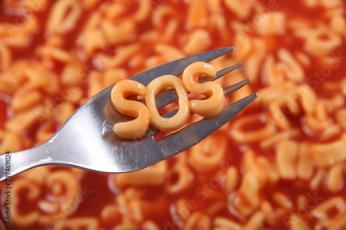 Spaghetti letter spelling the word SOS standing for Save Our Souls, with the letters held up on a fork, behind is the red tomato sauce. photo