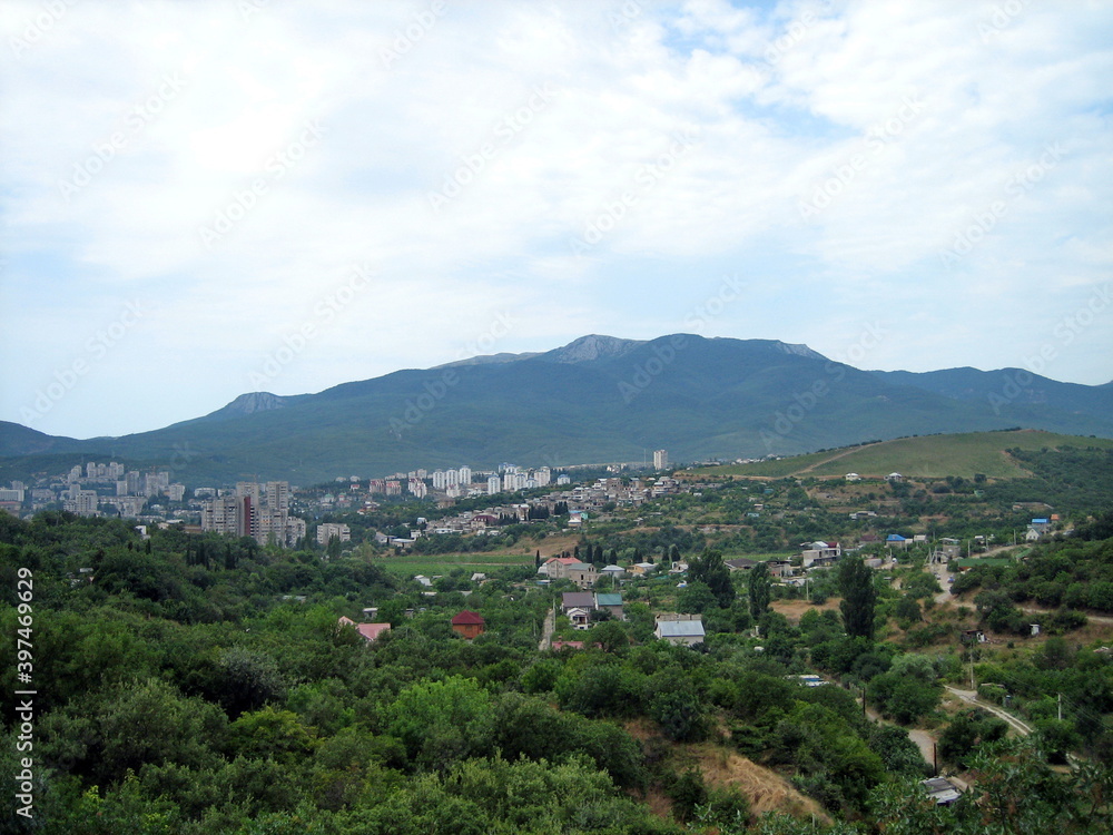 Obraz premium A village with houses and gardens in a picturesque valley surrounded by hills. Trees grow on the hillsides. Clouds float across the sky.