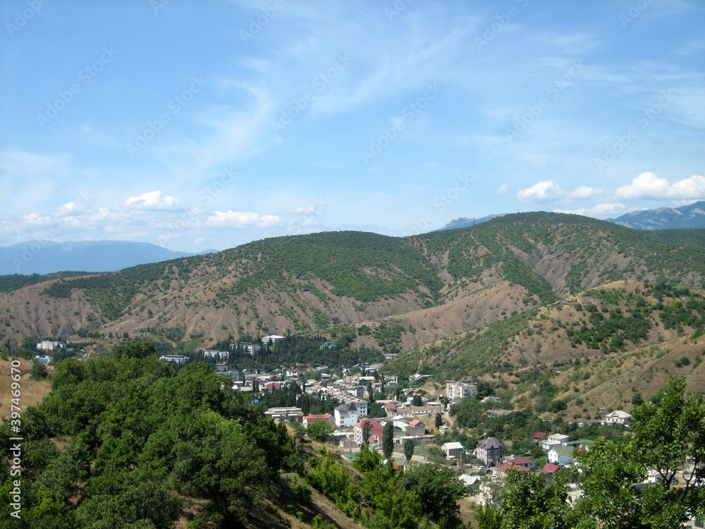 Obraz premium A village with houses and gardens in a picturesque valley surrounded by hills. Trees grow on the hillsides. Clouds float across the sky.