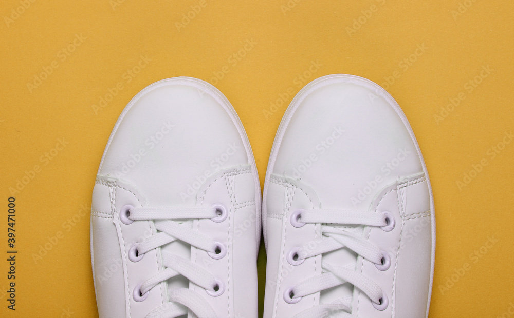 Stylish white sneakers on yellow paper background. Minimalistic fashion concept. Top view