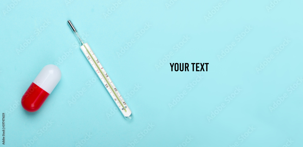 Pill capsule and thermometer on a blue pastel background with copy space. Top view Pill capsule and thermometer on a blue pastel background with copy space. Top view
